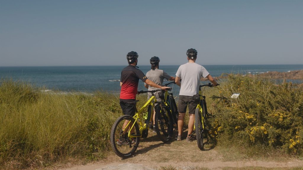 Three cyclists with e-bikes looking out to sea